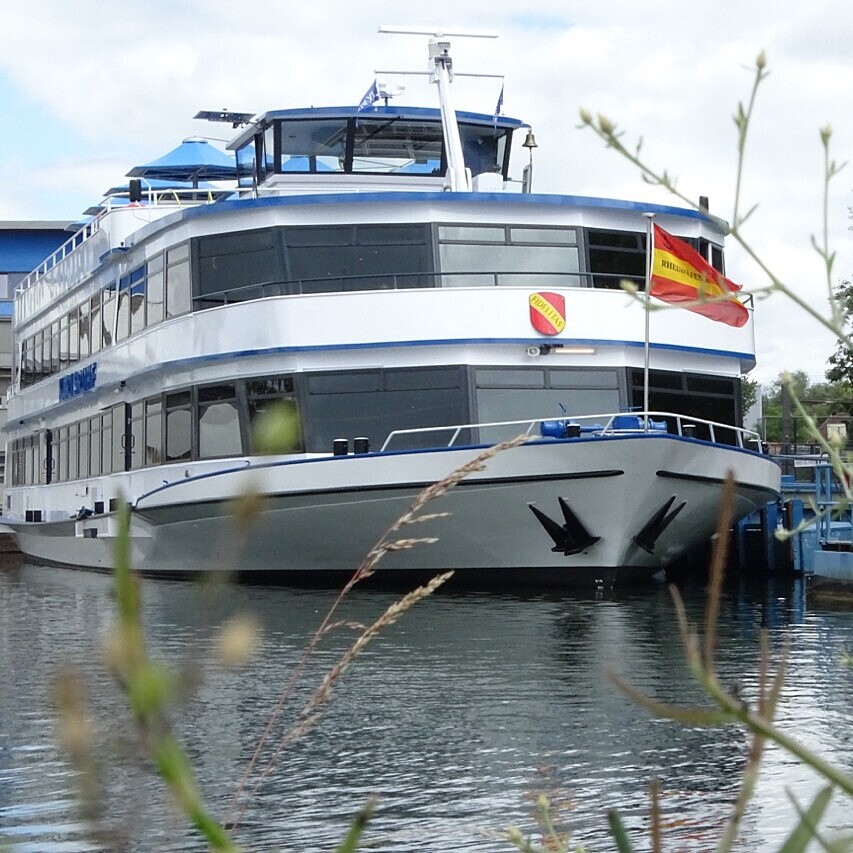 Fahrgastschiff MS Karlsruhe im Hafenbecken 2 des Rheinhafen Karlsruhe, am Steg liegend mit Hafenkränen und Industrieanlagen im Hintergrund.