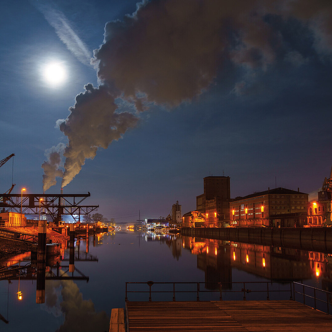 Hafenbecken 2 im Rheinhafen Karlsruhe bei Vollmondnacht, mit beleuchteten Industrieanlagen, Dampfschwaden und Spiegelungen im ruhigen Wasser.