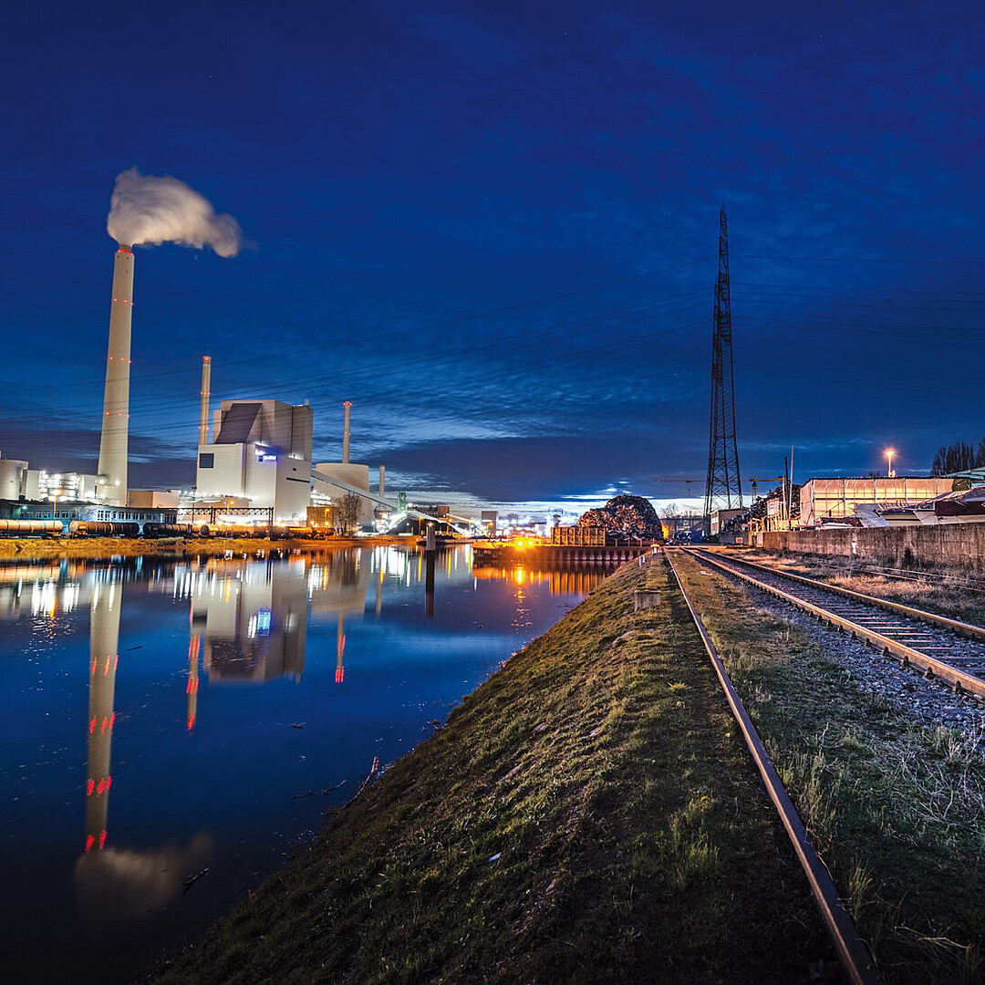 Nächtliche Ansicht der Trimodalität im Rheinhafen Karlsruhe mit Wasserstraße, Gleisanlagen und Industrieinfrastruktur, die die Verknüpfung von Schiff, Bahn und Straße zeigt.