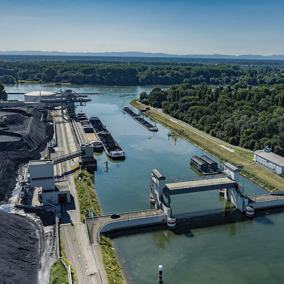 Luftaufnahme des Rheinhafen Karlsruhe mit Blick auf das Hafensperrtor, Hafenbecken, Schleusenanlage und angrenzende Grünflächen entlang des Rheins.