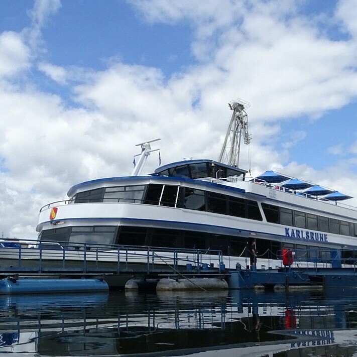 Fahrgastschiff MS Karlsruhe im Hafenbecken 2 des Rheinhafen Karlsruhe, am Steg liegend mit Hafenkränen und Industrieanlagen im Hintergrund.