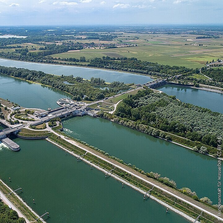 Luftaufnahme der Staustufe Iffezheim am Rhein mit Schleusenanlagen, Wehr und umliegender Landschaft als Zielort für Ausflugsfahrten.