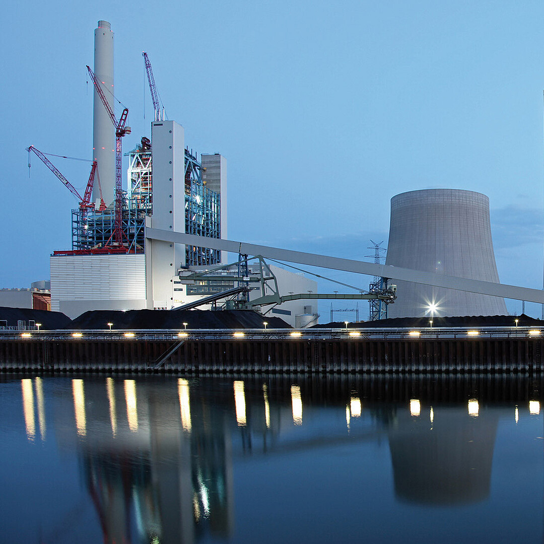 Abendliche Industrieansicht im Rheinhafen Karlsruhe mit Kraftwerksanlagen, Kränen und Spiegelungen im Hafenbecken bei Dämmerung.